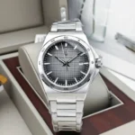 Silver stainless steel wristwatch with a textured gray dial, date window at 3 o'clock, and a brushed bezel, displayed in a box.