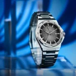 Close-up of a stainless steel wristwatch with a black textured dial, date window at 3 o'clock, against a blue background.