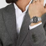 Man wearing a gray blazer and white shirt, showcasing a silver wristwatch on his left wrist.
