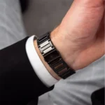 Close-up of a metal link watch bracelet on a man's wrist, with a white shirt cuff and black suit sleeve visible.