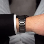 Close-up of a black metal wristwatch on a man's left wrist, with a white dress shirt cuff showing beneath the sleeve.