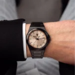 Close-up of a black metal Maserati wristwatch with a beige textured dial and date window on a suited arm.