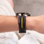 Wristwatch with black strap and a yellow stripe on a metal case, worn on a forearm.