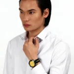 Man in a white shirt adjusts his collar, wearing a bold yellow-dial wristwatch with a black strap on his left wrist.