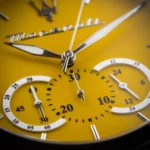 Close-up of a yellow chronograph watch face with silver hands and multiple subdials showing seconds and minutes