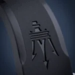 Close-up of a dark over-ear headphone earcup with a stylized logo featuring an M and horizontal lines on the surface
