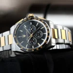 Close-up of a two-tone stainless steel and gold wristwatch with a black textured dial and tachymeter bezel on black fabric