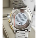 Back of a stainless steel wristwatch with a circular multilingual instruction sticker reading ATTENTION! Tighten crown down the crown.