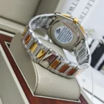 Two-tone metal wristwatch with silver and gold links displayed on a cushioned stand in a box, showing a polished bracelet and case back.